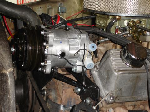 1977 Ford F-150 - Close-up view of an air conditioning compressor installed in an engine bay, with visible belts, pulleys, and engine components.