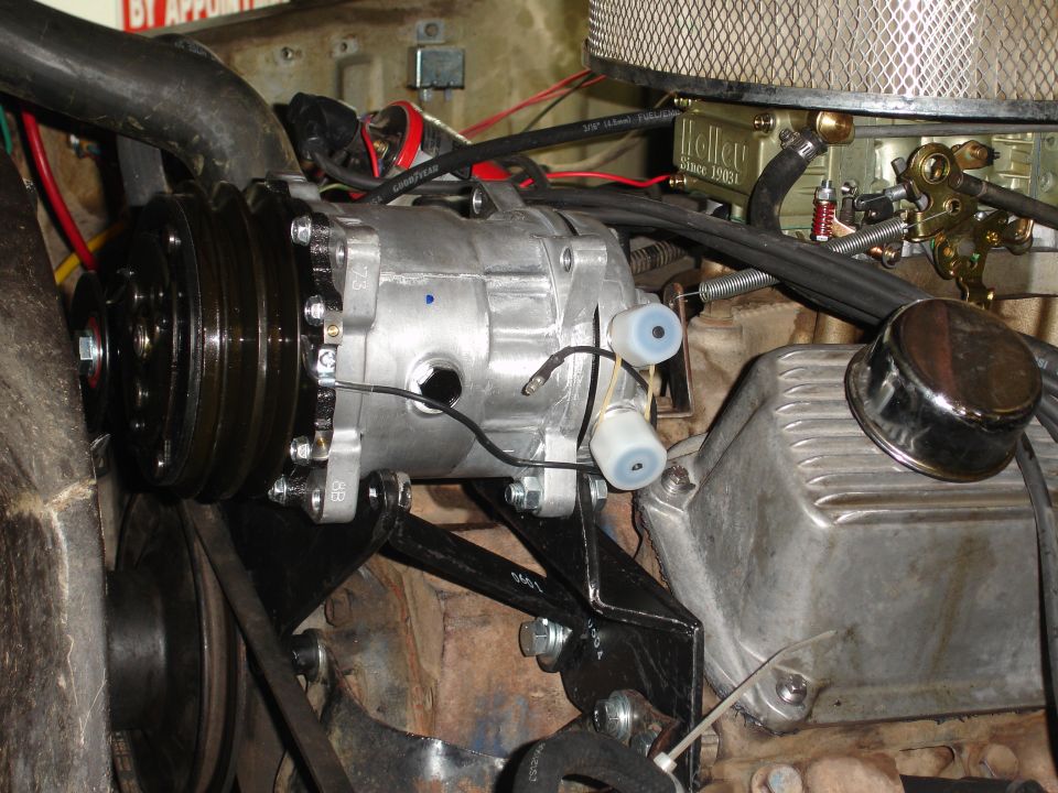 Air conditioning compressor mounted in engine bay, showing belts and pulleys