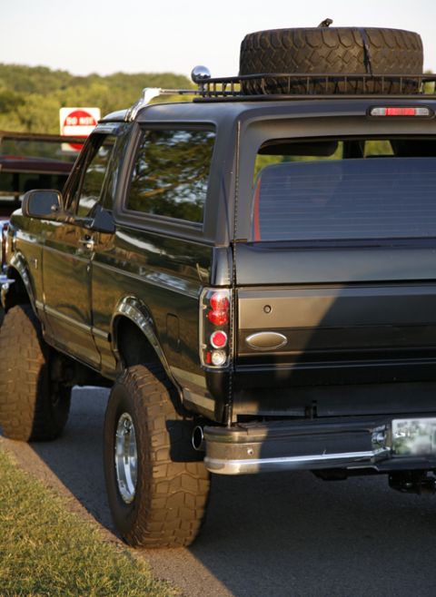 1995 Ford Bronco - Three-quarter rear view of a lifted black Ford Bronco full-size SUV with the removable hardtop in place, mud-terrain tires on chrome wheels…
