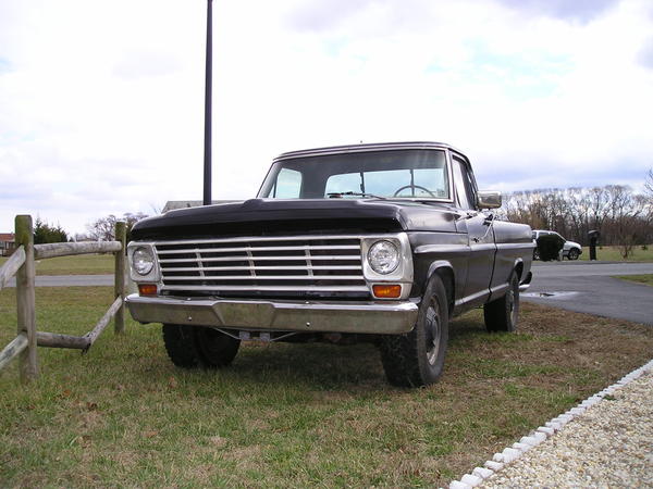 Dark 1967 Ford F-250 pickup parked on grass by a wooden fence, front three-quarter view