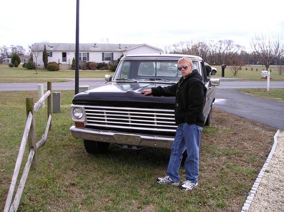 Man leaning on hood of vintage Ford pickup with black front end and chrome grille, parked on grass