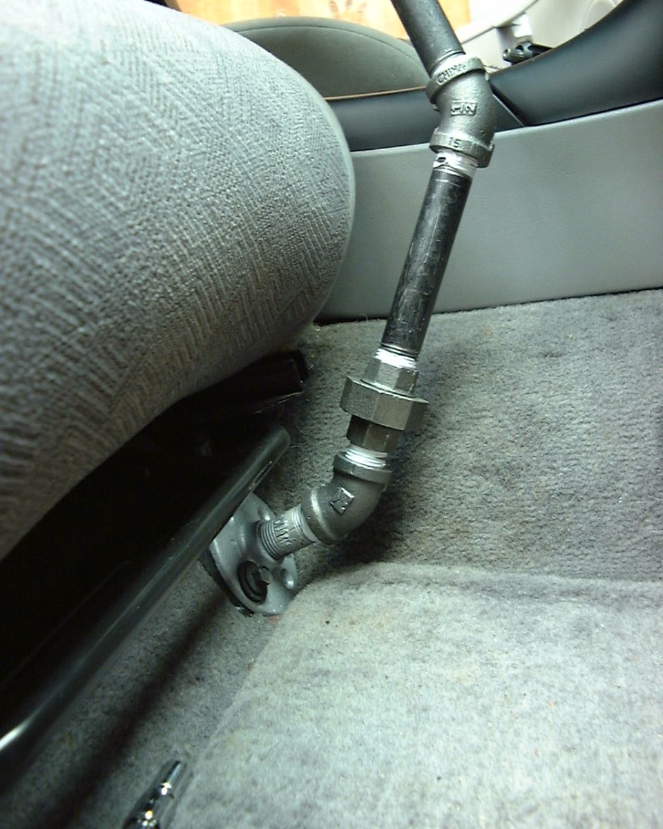 DIY black iron pipe fitting assembly with union and flange mounted beside gray seat on carpeted floor