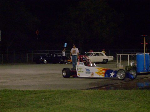 1991 Ford Mustang - A dragster with a patriotic theme sits on the track, with other vehicles visible in the background.