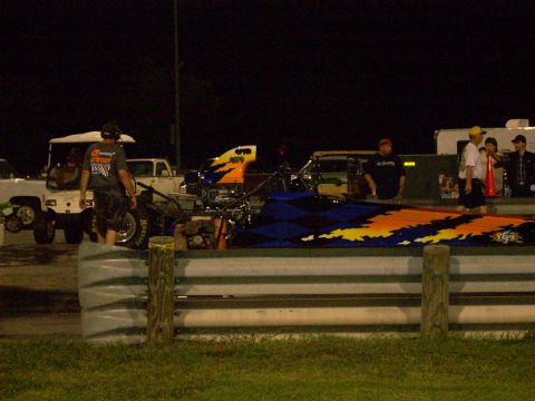 1991 Ford Mustang - A dragster with vibrant flame graphics is visible on a track at night, with several people and other vehicles in the background.
