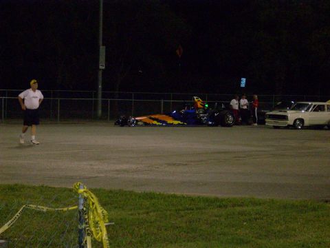 1991 Ford Mustang - A drag racing car and a sedan are parked on a track at night, with a person standing in the foreground.