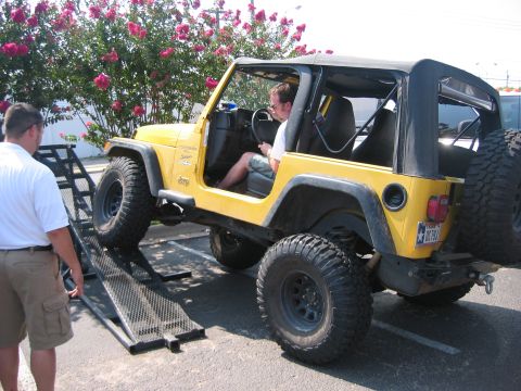 2001 Jeep Wrangler - A yellow Jeep Wrangler TJ with doors off, soft top up and a black roll cage is driven up ramps onto a trailer in a sunlit parking lot while…