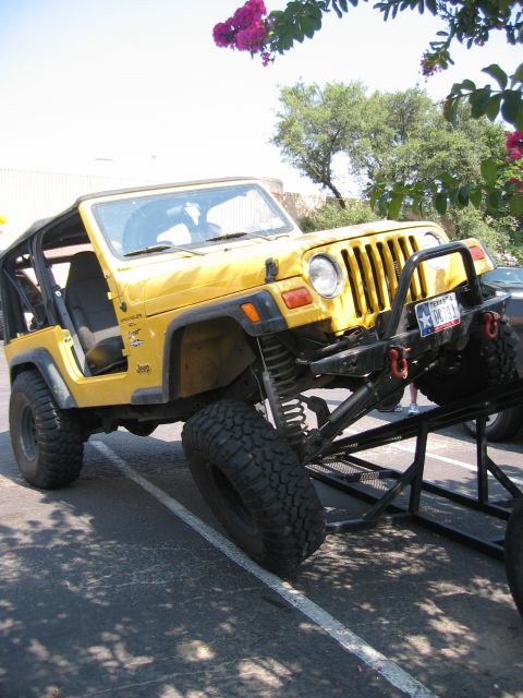 2001 Jeep Wrangler - Yellow Jeep Wrangler TJ Sport 4.0L, doors removed and soft top down over a roll bar, flexing its lifted front suspension on a parking-lot o…