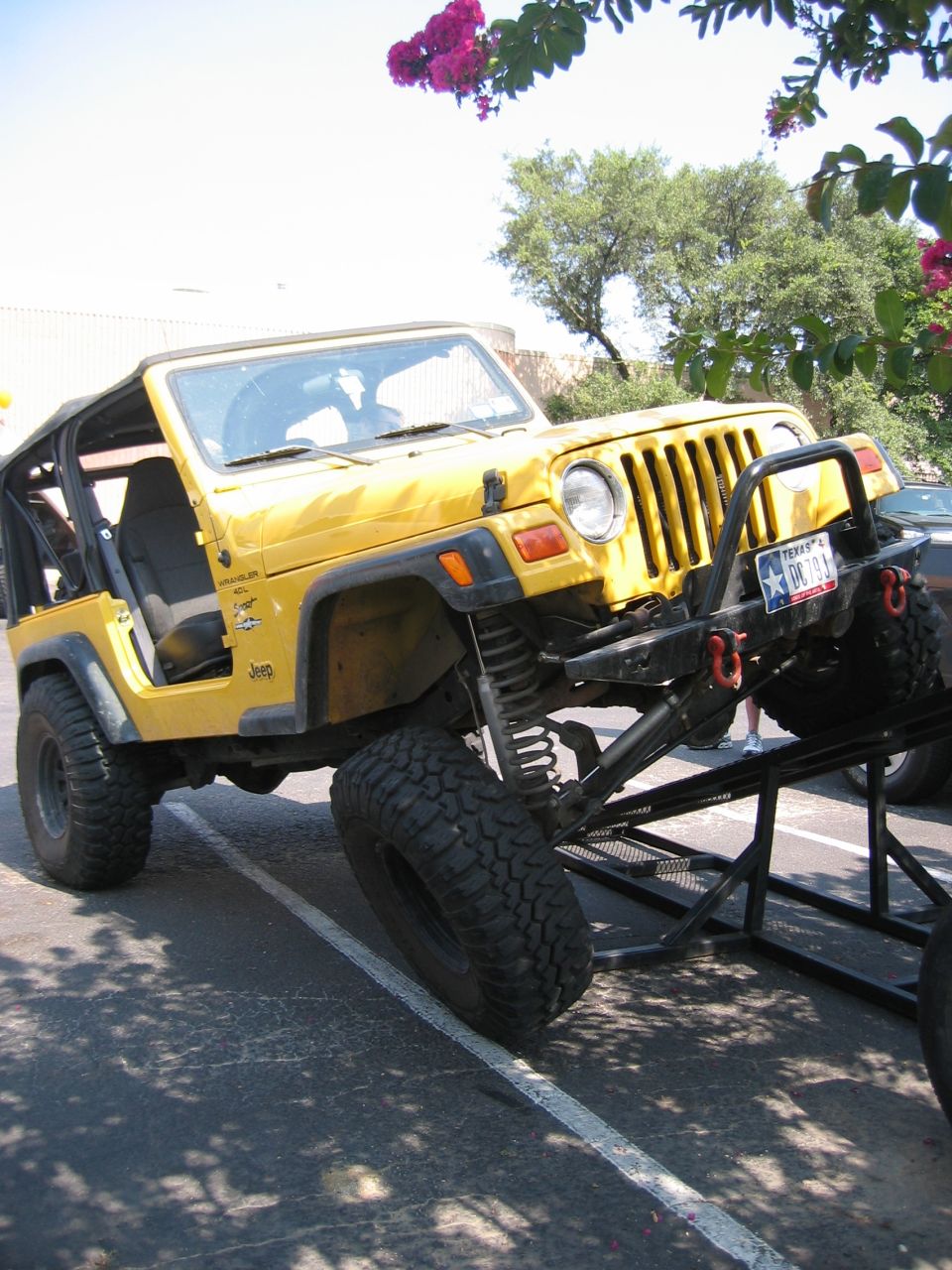 Yellow Jeep Wrangler TJ on lift kit and mud tires flexing over a steel ramp at an outdoor event