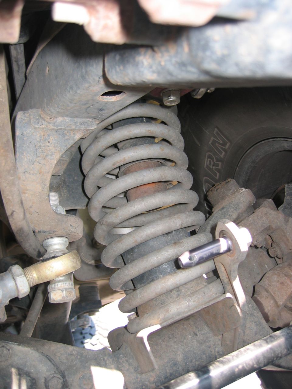 Close-up of coil spring, shock, tie-rod end and control arm bracket on a solid axle