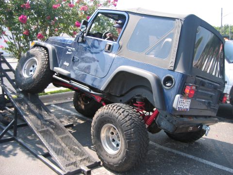 2001 Jeep Wrangler - A blue Jeep Wrangler is shown with its front tires on a ramp, its lifted suspension and off-road tires.