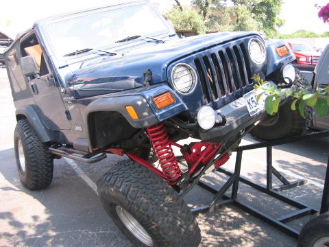 2001 Jeep Wrangler - A blue 2001 Jeep Wrangler is displayed with its front end elevated on a metal stand, revealing its modified suspension.