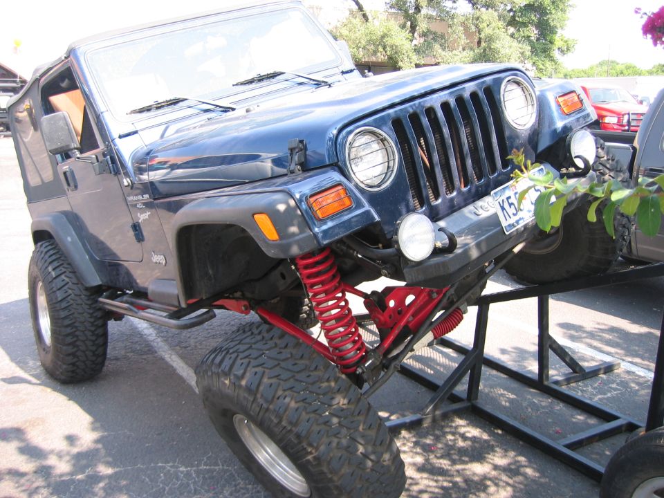 Blue 2001 Jeep Wrangler with lifted suspension and large tires, angled on a display stand
