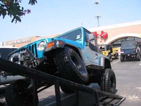 2001 Jeep Wrangler - A blue 2001 Jeep Wrangler TJ is positioned on a ramp in a parking lot, with other Jeeps visible in the background.