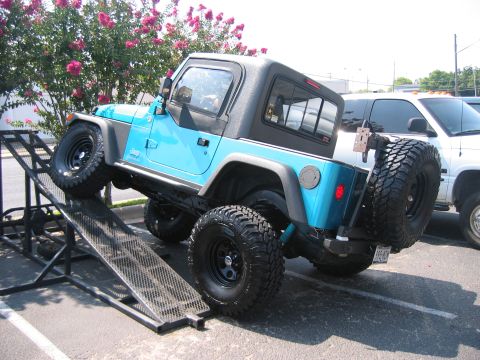 2001 Jeep Wrangler - A blue Jeep Wrangler is positioned on a metal ramp, with a spare tire mounted on the rear.
