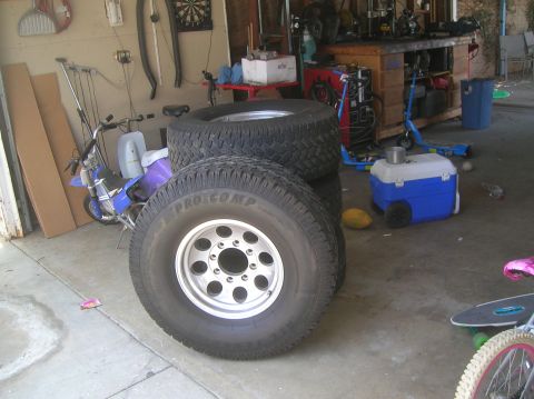 1985 Ford Bronco - Four Pro Comp tires are stacked in a garage, with a dirt bike and other items in the background.
