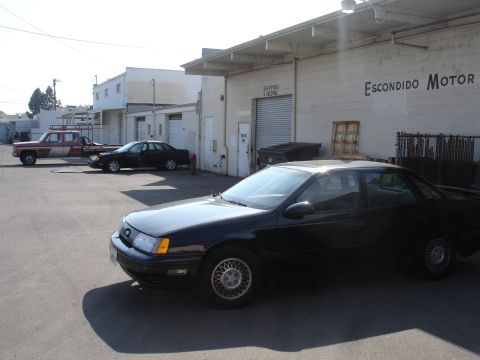 1991 Ford Taurus - A black 1991 Ford Taurus is parked in front of a commercial building with a sign that reads 'ESCONDIDO MOTOR'.