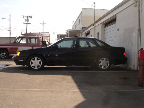 1991 Ford Taurus - A black 1991 Ford Taurus is parked in front of a building, with a red pickup truck visible behind it.