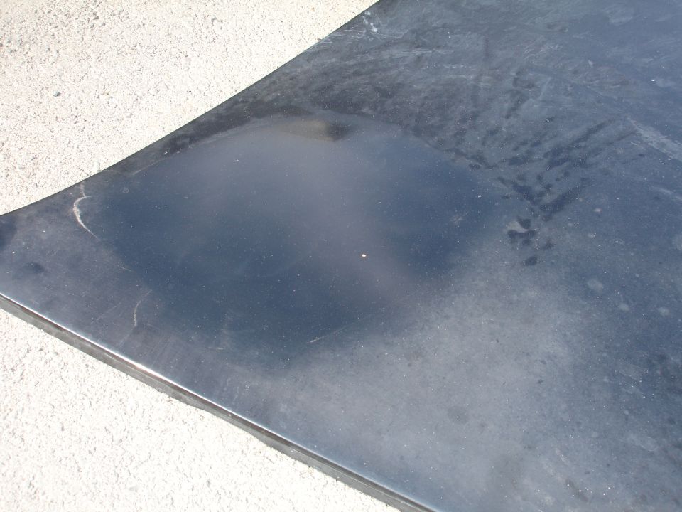 Black car hood with scuffs and water marks, viewed from a high angle
