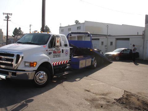 1991 Ford Taurus - A tow truck is preparing to load a dark sedan onto its flatbed in front of a commercial building.