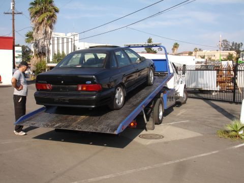 1991 Ford Taurus - A black 1991 Ford Taurus sedan is loaded onto a tow truck for transport.
