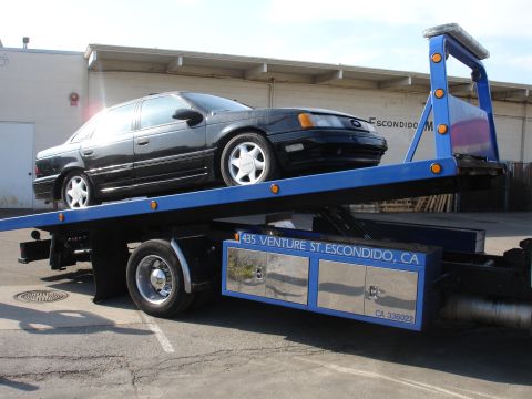 1991 Ford Taurus - A black 1991 Ford Taurus is loaded onto a tow truck.
