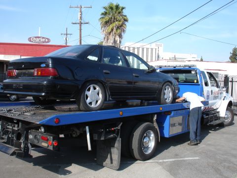 1991 Ford Taurus - A tow truck operator secures a black 1991 Ford Taurus onto the flatbed.