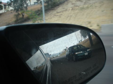1991 Ford Taurus - A dark green sedan is reflected in the side mirror of a vehicle on the highway.