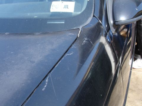 1991 Ford Taurus - Close-up of a black car's fender and windshield, showing damage and a July sticker.