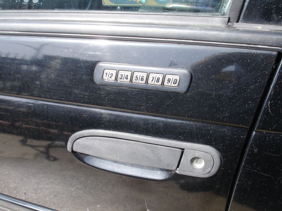 Close-up of a black car door with a factory keypad entry system above the handle