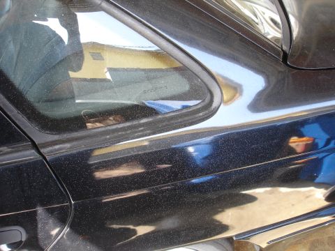 1991 Ford Taurus - Close-up of a black car's side door, showing dust and reflections.