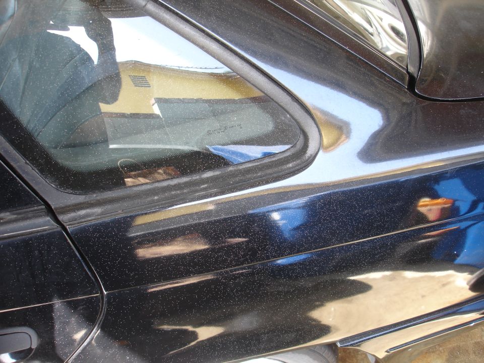 Black car door with dust specks and reflection of a yellow building