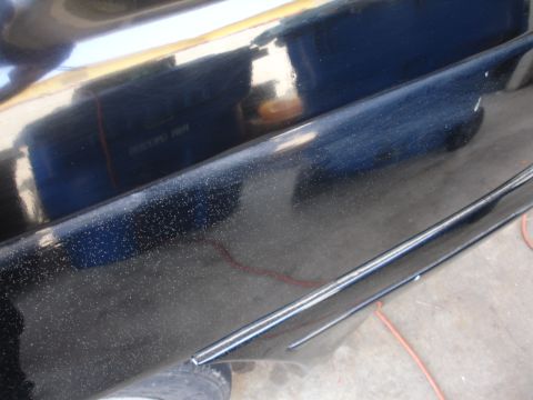 1991 Ford Taurus - Close-up of a black car door showing chrome trim and a textured surface with small imperfections.