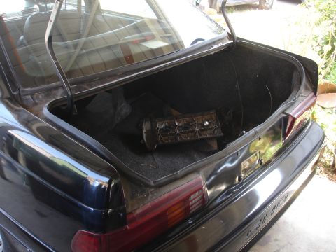 1991 Ford Taurus - Trunk interior of a black car containing a car part and other items.