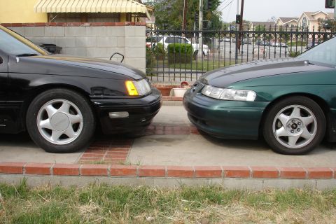 1991 Ford Taurus - Two sedans are parked facing each other on a paved driveway.