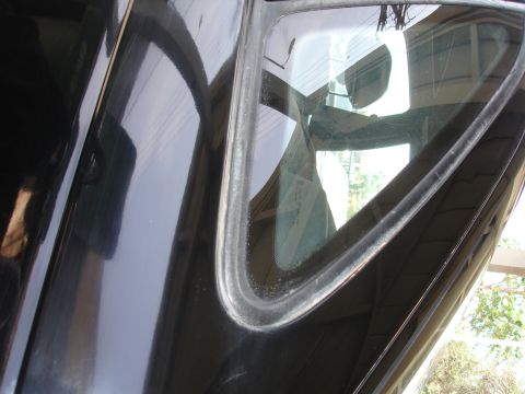 1991 Ford Taurus - Close-up of a black car's rear quarter window frame, showing reflections.