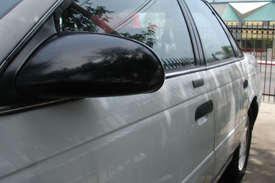 Side view of a white 1992 Ford Taurus sedan, showing the door handle and side mirror