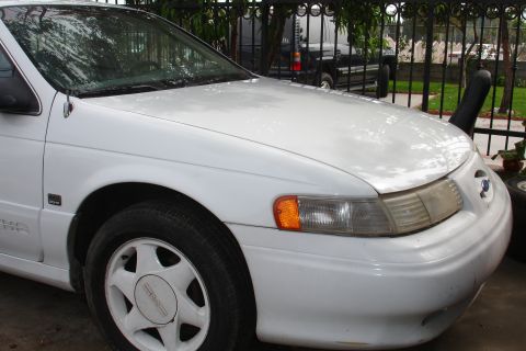 1992 Ford Taurus - The front end of a white 1992 Ford Taurus is visible, showing the headlight and grille area.