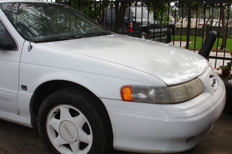 White Ford Taurus sedan front three-quarter view by black fence
