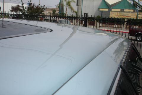1992 Ford Taurus - The top of a light-colored car shows water trails and a sunroof, with a building and fence visible behind it.