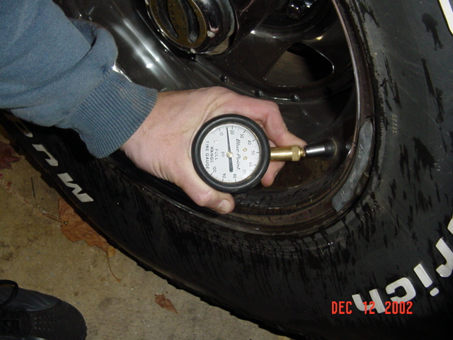 Hand holding a dial tire-pressure gauge against a BFGoodrich mud tire on a black wheel