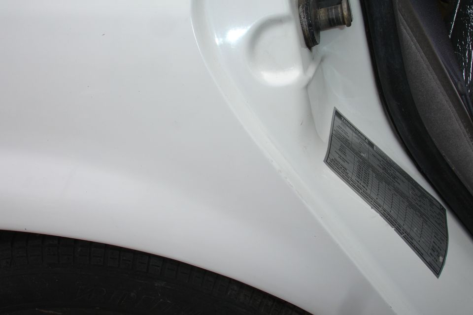 White car door jamb with a black tire and a VIN sticker
