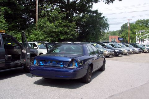 2001 Ford Crown Victoria - A blue sedan sits in a parking lot, its rear end showing damage and exposed components.