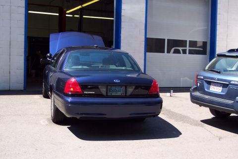 2001 Ford Crown Victoria - Rear view of a dark blue 2001 Ford Crown Victoria with its hood open, parked next to a blue SUV.