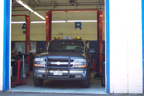 2001 Ford Crown Victoria - A dark SUV with a push bar and emergency lights is parked inside a garage with a vehicle lift.