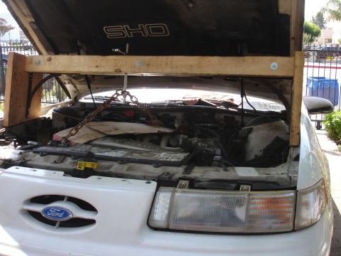 1992 Ford Taurus - The engine bay of a white Ford Taurus SHO is visible, supported by a wooden beam and chain hoist.