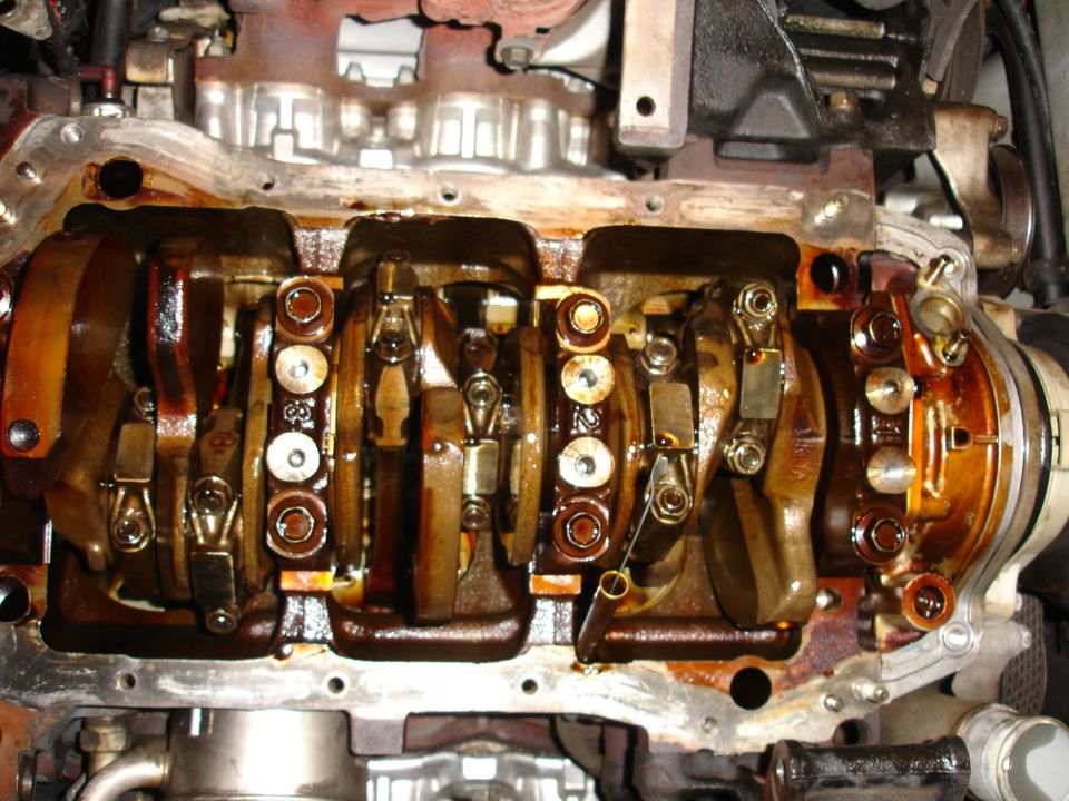 Engine crankshaft with connecting rods, covered in oil. Close-up view