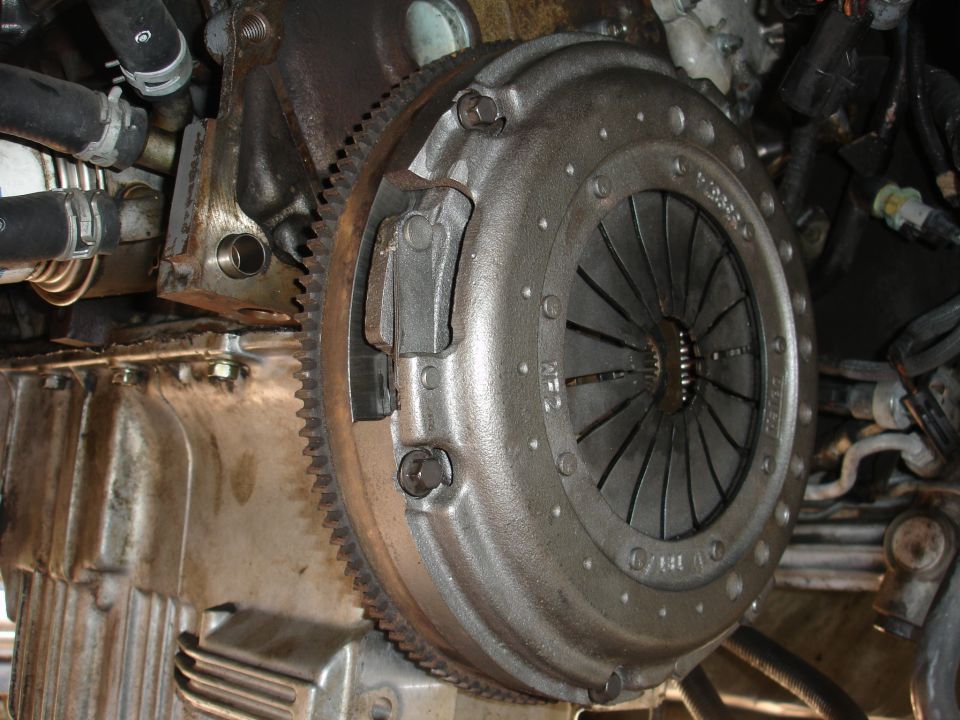 Clutch assembly and flywheel on a vehicle engine, showing metal parts and hoses
