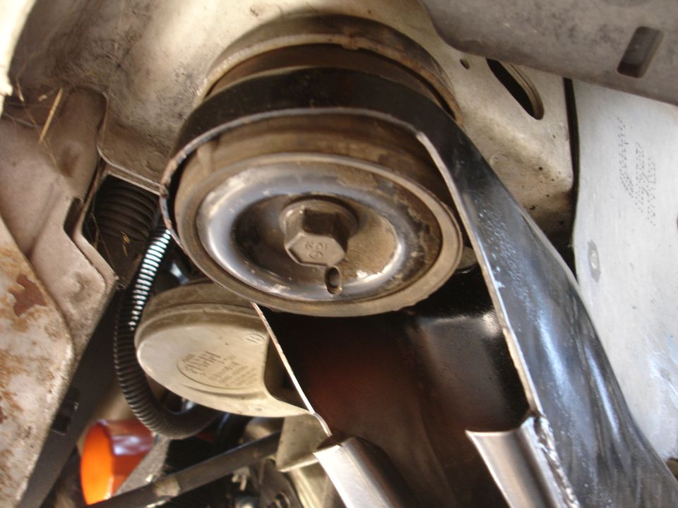 Close-up of a hex bolt in center of engine pulley with brackets and spring