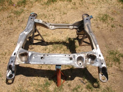 1992 Ford Taurus - A bare metal subframe assembly is supported by jack stands on a grassy area.
