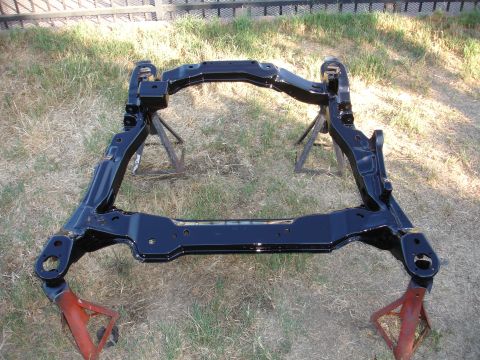1992 Ford Taurus - A black subframe, likely for a vehicle's suspension, is shown resting on jack stands in a grassy outdoor area.